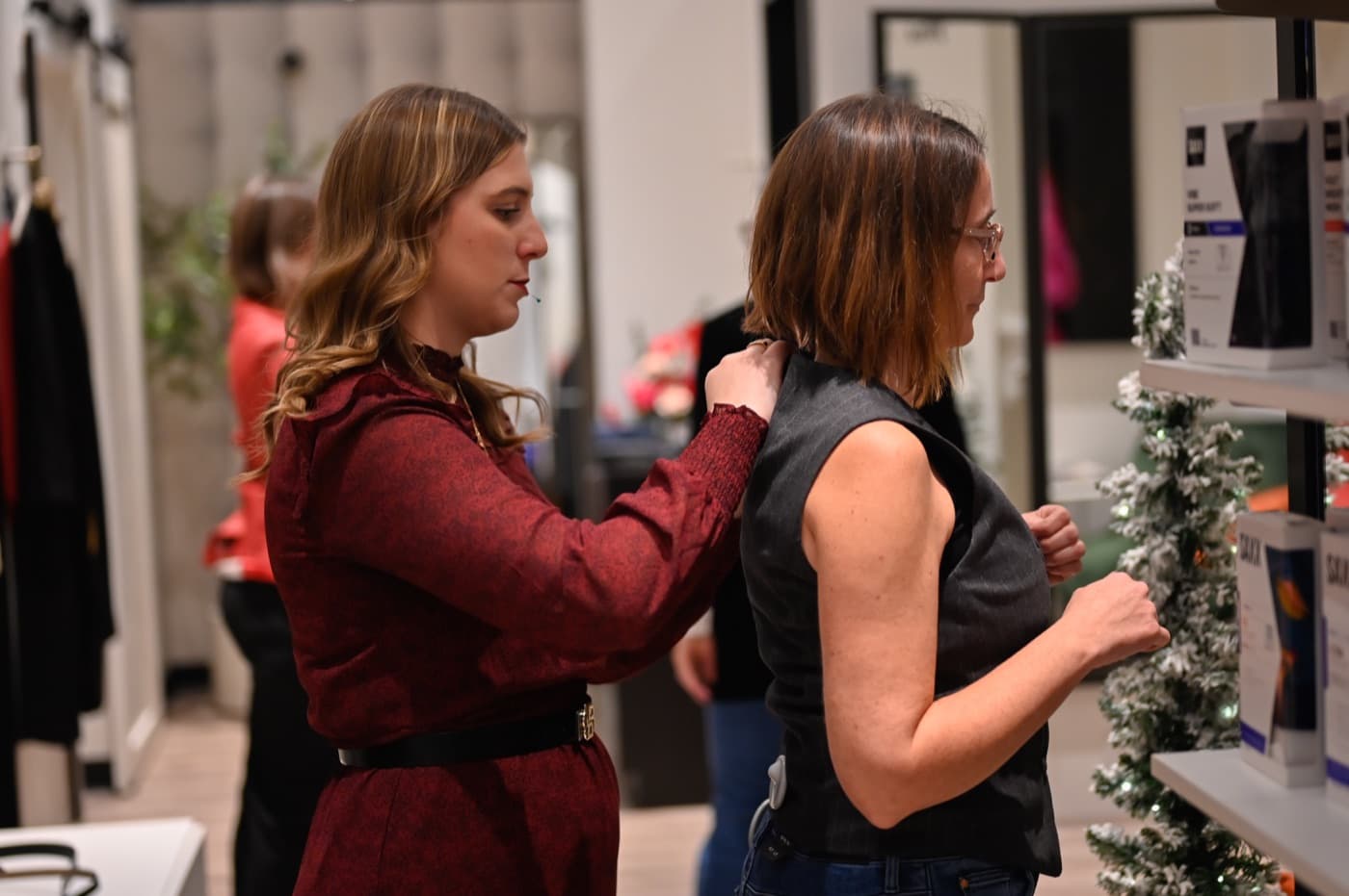 Une styliste ajuste un gilet sur une participante dans la boutique M2